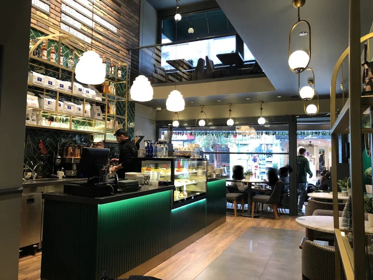 Le Petit Moulin'in barı ve pastane vitrini: espresso makinesi, cam vitrinde tatlılar, yeşil karo duvar ve pirinç sarkıt aydınlatmalar