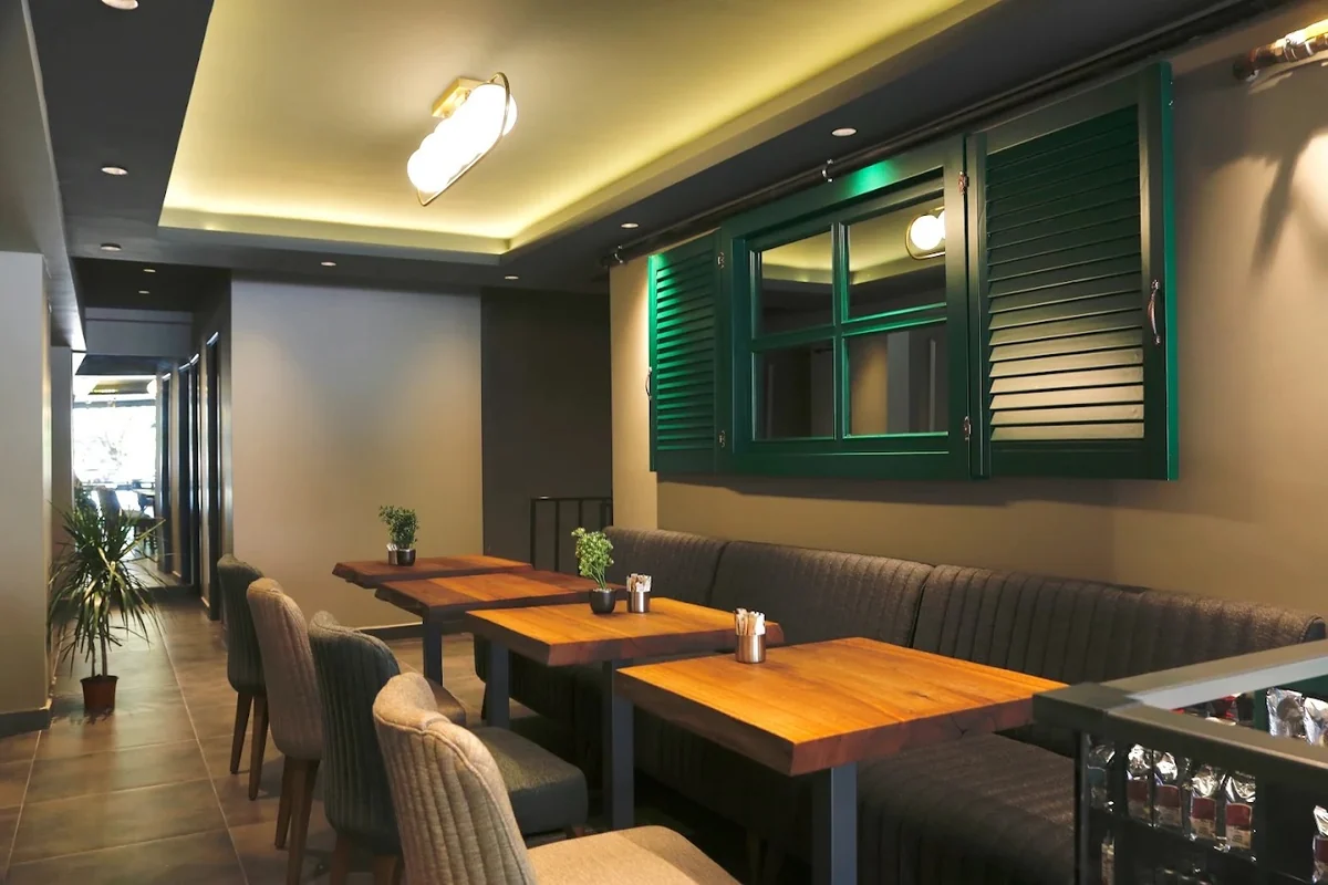 Le Petit Moulin'in panjurlu salonu: duvar boyunca uzanan bank, masif ahşap masalar ve koyu yeşil ahşap panjurlar